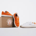 Jägermeister x Flowers For Society The Curt Sneaker i orange mocka och vitt läder, båda färgvarianter uppställda med förpackning