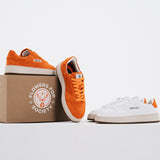 Jägermeister x Flowers For Society The Curt Sneaker i orange mocka och vitt läder, båda färgvarianter uppställda med förpackning