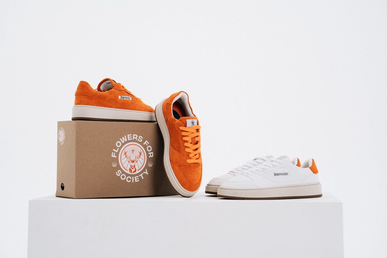 Jägermeister x Flowers For Society The Curt Sneaker i orange mocka och vitt läder, båda färgvarianter uppställda med förpackning