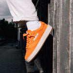 Jägermeister x Flowers For Society The Curt Sneaker i orange mocka, sidovy på fot mot vägg utomhus